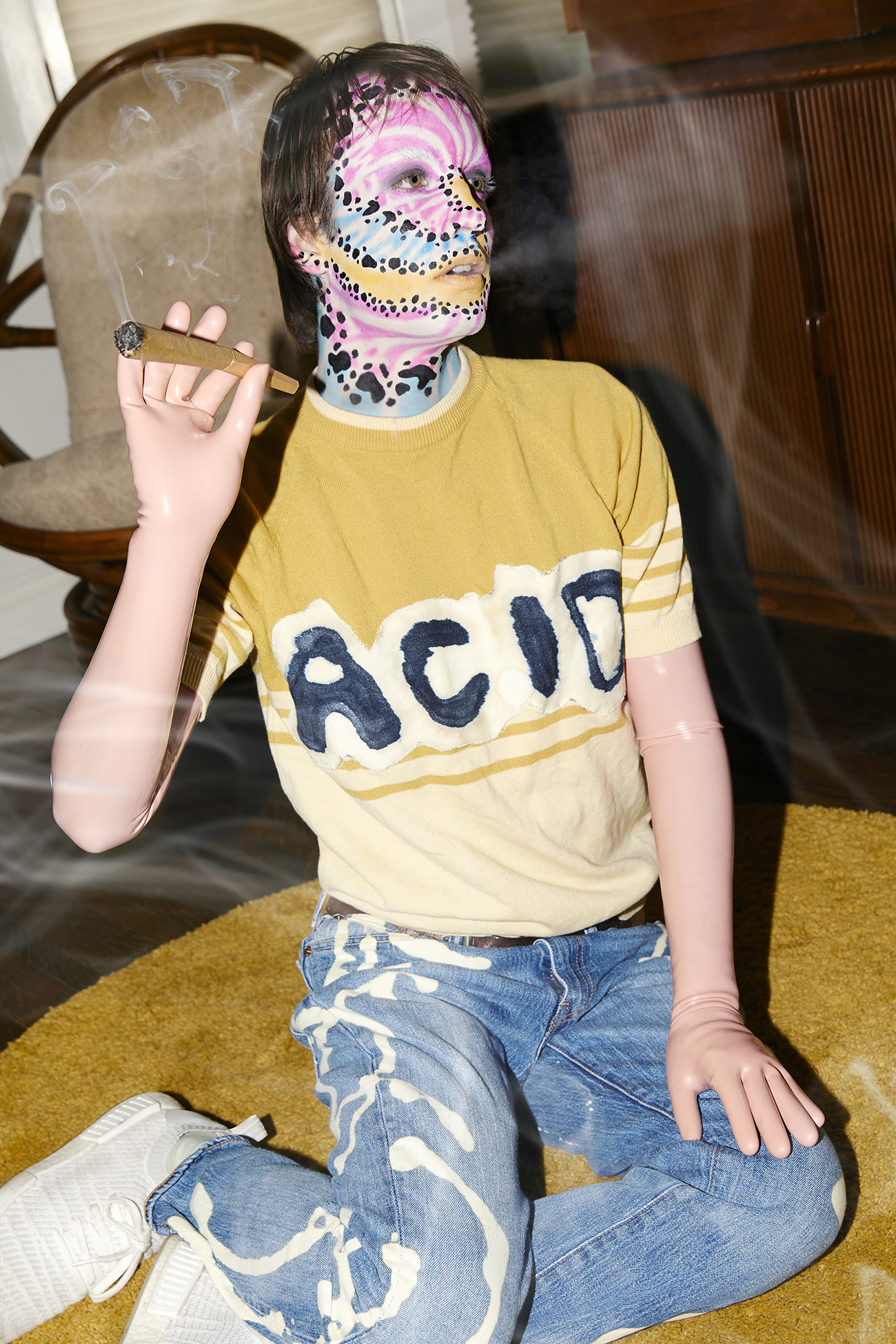 Jesse in tie-dye makeup sitting and smoking a blunt in a home